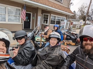 A group of people in helmets stand among motorcycles and smile. 